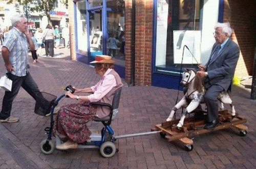 Papy et Mamy en balade... elle en fauteuil roulant electrique et lui sur un cheval de bois, attache derriere